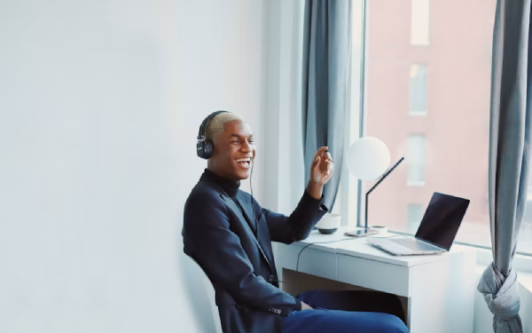 Man sitting by a window wearing headphones, smiling and gesturing